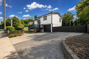 A two-story house with a front deck, a garage, and a gravel driveway.