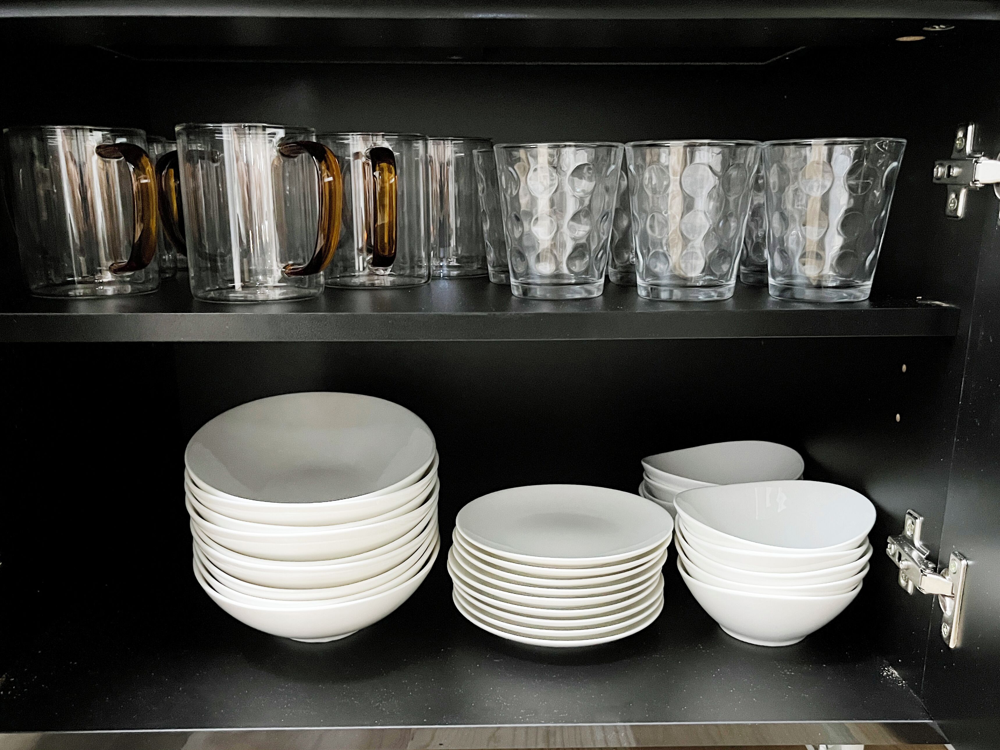 A storage unit with clear glassware and white plates.