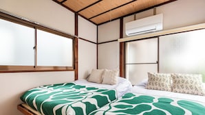 A room with a bed, two pillows, a window, and an air conditioning unit.