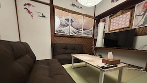 A living room with a brown sofa, a wooden coffee table, a television, and Japanese artwork on the wall.