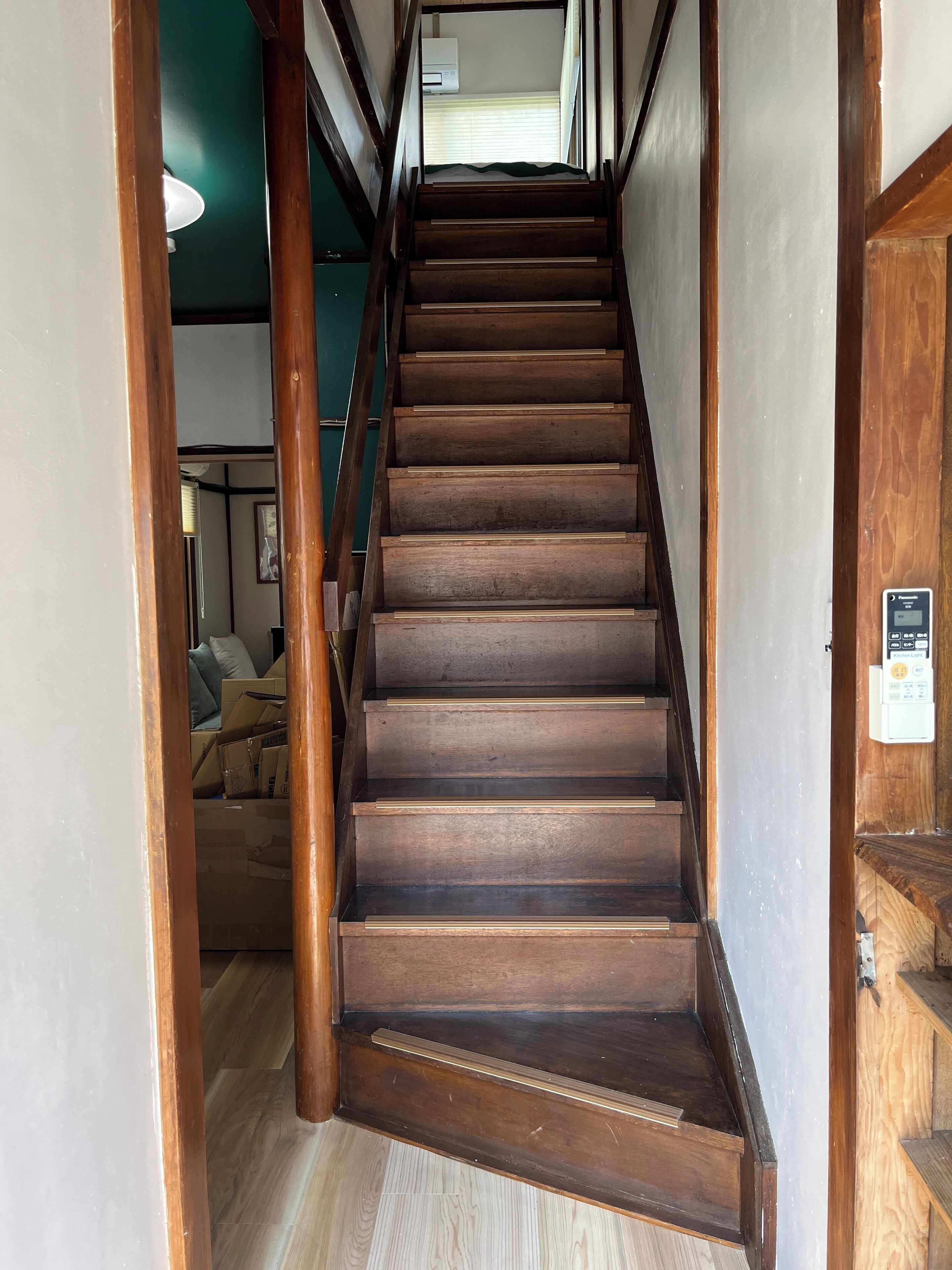 A wooden staircase with a handrail, leading to a room with a bed and a window.
