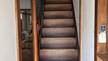 A wooden staircase with a handrail, leading to a room with a bed and a window.