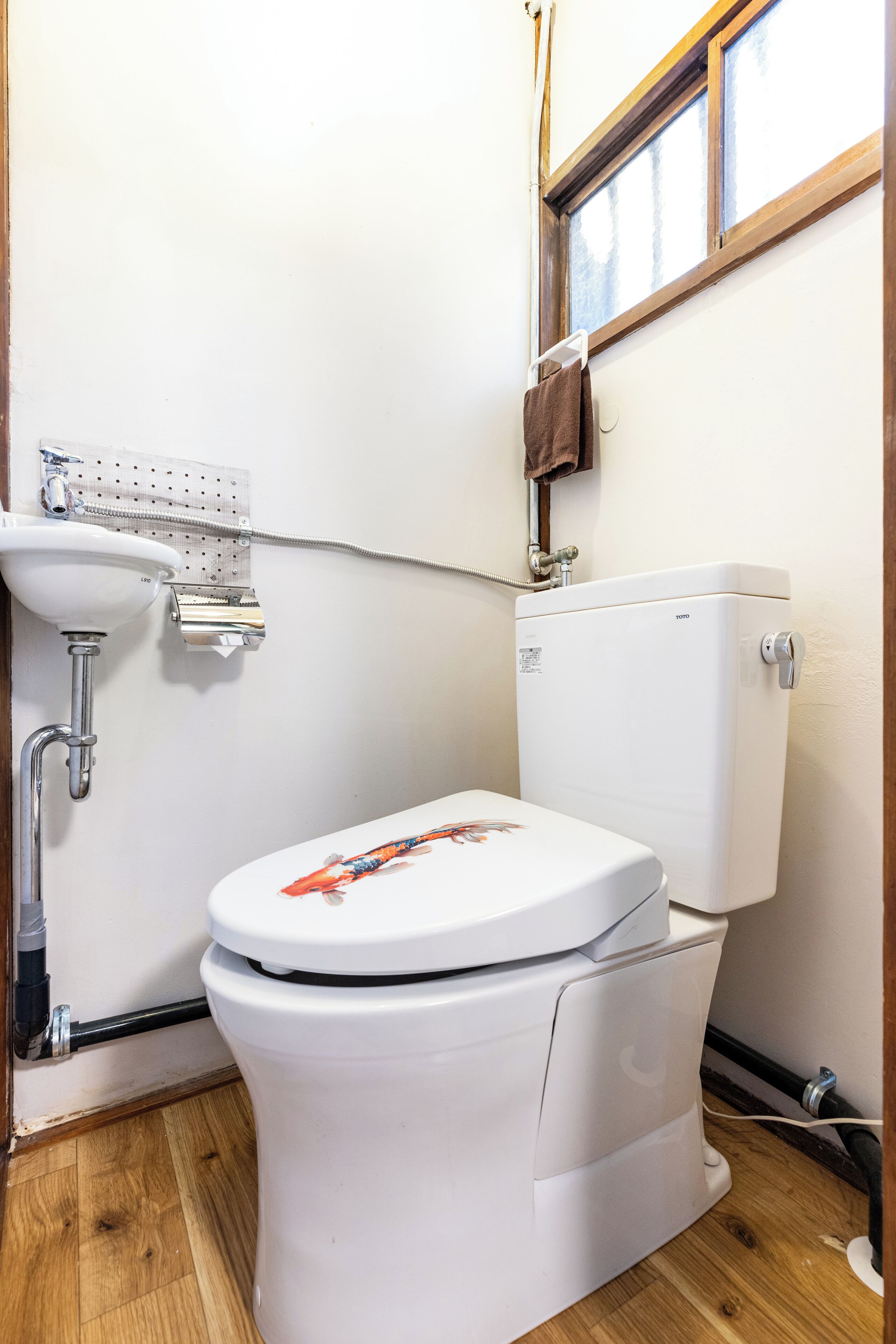 Et lille, rent badeværelse med toilet, håndvask og et vindue.