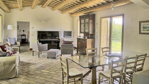 Amplia sala de estar con mesa de vidrio, sillas de mimbre, un piano y chimenea.