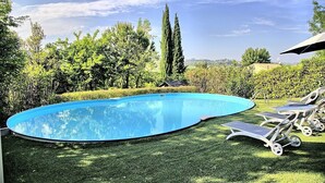Una piscina de borde curvo, rodeada de césped cuidado y varios árboles.