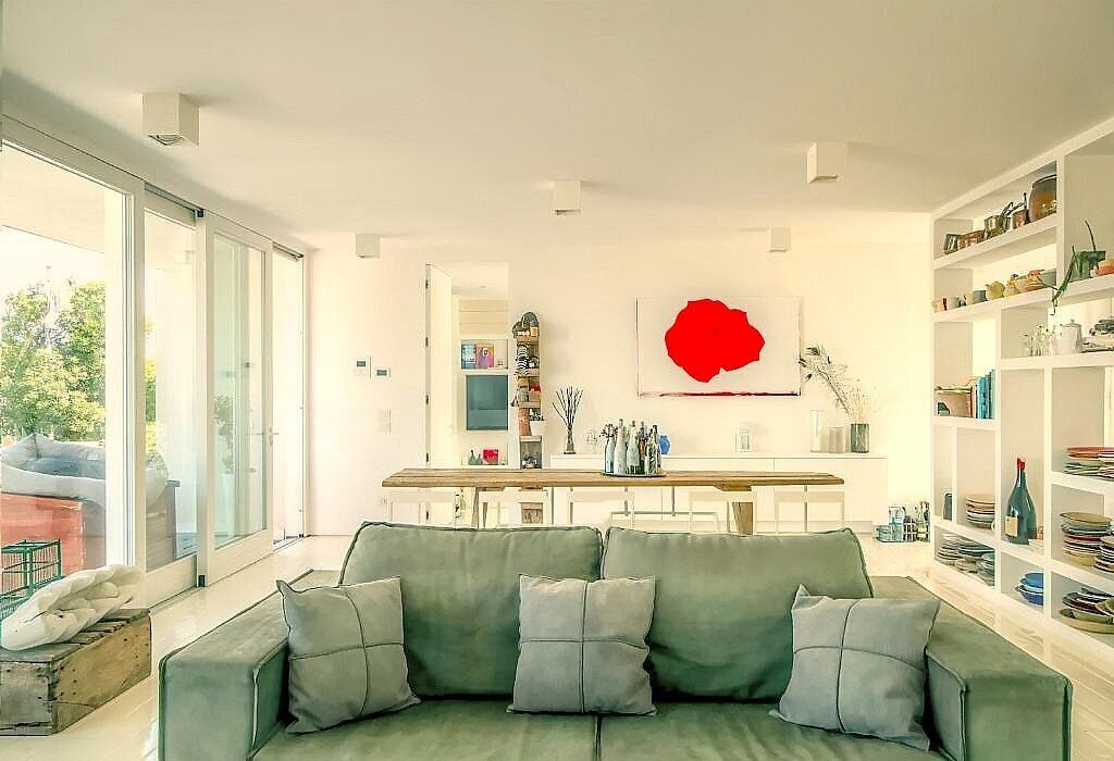 Uma sala de estar moderna com um sofá cinzento, um quadro abstrato vermelho e uma área de jantar com mesa e cadeiras de madeira.