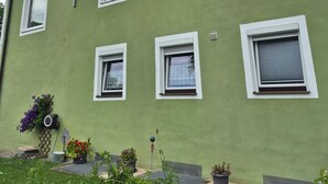 A green building with multiple windows, a slanted roof, and a small garden area with potted plants. - Vacation apartment with mountain view for max. 2 persons, 36 sqm (Bad Reichenhall)