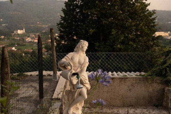 Una estatua en un entorno al aire libre, con una cerca y árboles de fondo.