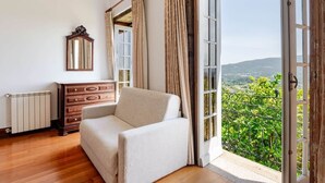 Habitación con sofá, cómoda, espejo y un ventanal con vistas a la vegetación.