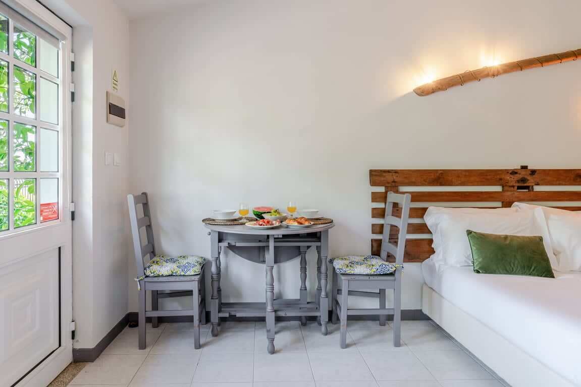A room with a dining table set for two, a wooden headboard, and a white sofa with a green pillow.