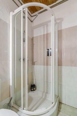 A shower enclosure with a glass door, a white bathtub, and a showerhead.