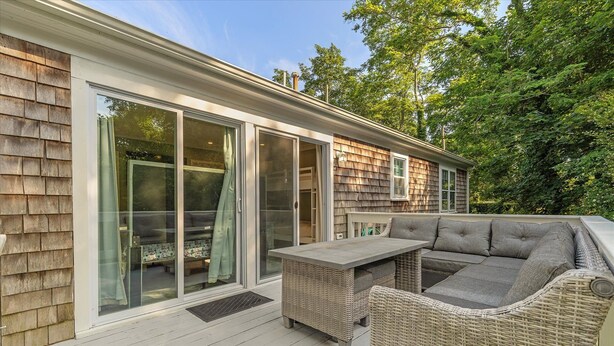 A covered deck with a wicker sofa and table, large sliding glass doors, and a shingled exterior.