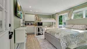 A bedroom with bunk beds, a desk, and a kitchenette.