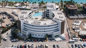 Un hotel moderno con piscina circular, vistas a la playa y aparcamiento.