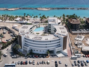 Ein modernes Hotel mit einem runden Pool, Blick auf den Strand und einem Parkplatz.
