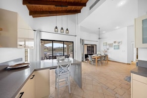 A modern kitchen with a large island, a dining area with a view, and a pool visible through the window.