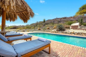 A poolside area with lounge chairs and a thatched roof structure.