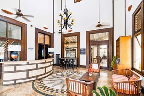 Un hall d’entrée avec un comptoir de réception, un espace salon, un lustre, des ventilateurs de plafond et une enseigne indiquant « Aruba Sotheby’s ».