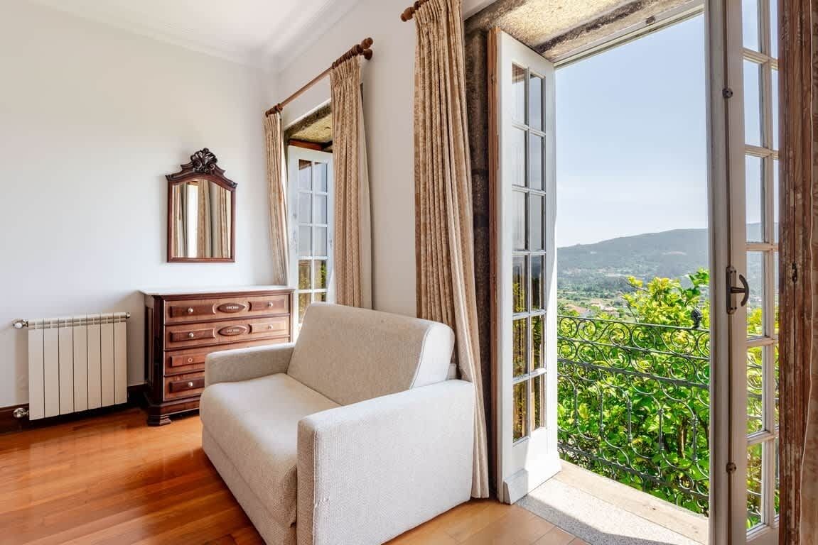 A room with a sofa, a dresser, a mirror, and a large window with a view of greenery.