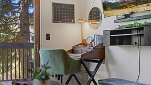 Habitació amb escriptori, cadira verda, calendari penjat a la paret, rellotge i finestra amb vista a arbres i muntanyes.