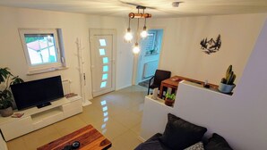 A modern living room with a flat-screen TV, wooden coffee table, dark sofa, and a dining area with a table and chairs. - Apartment "Liana" with view to the castle (Hechingen)
