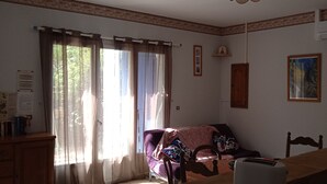 A room with a dining table, a purple sofa, a wooden cabinet, and a window with curtains. - Comfortable country house with swimming pool (Saint-Rémy-de-Provence)