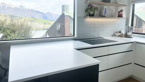 A modern kitchen with a large window, white cabinetry, and a view of mountains.