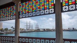 Vista desde un área techada con barandilla, que da al puerto con barcos y un edificio moderno al fondo.