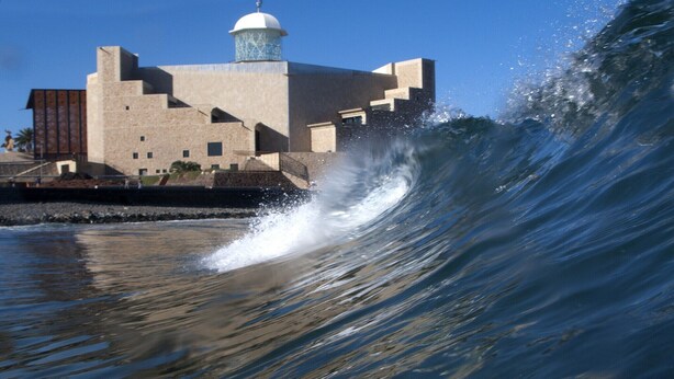 A wave crashing against a building with a dome and a staircase leading up to it.