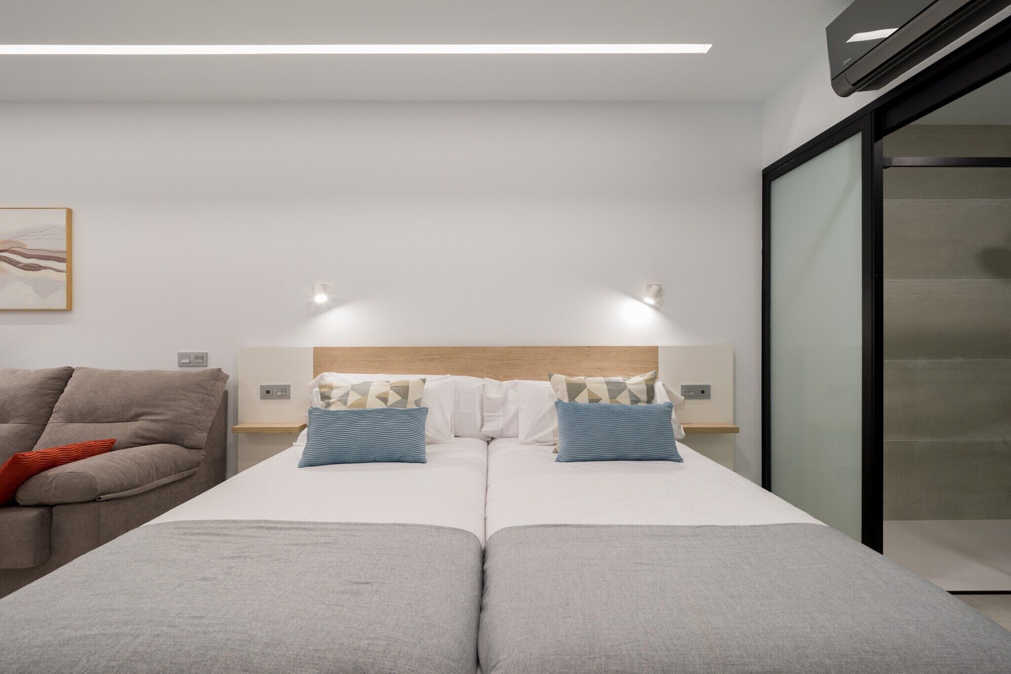 Moderni hotellihuone, jossa on suuri sänky, sohva ja lasiseinä.