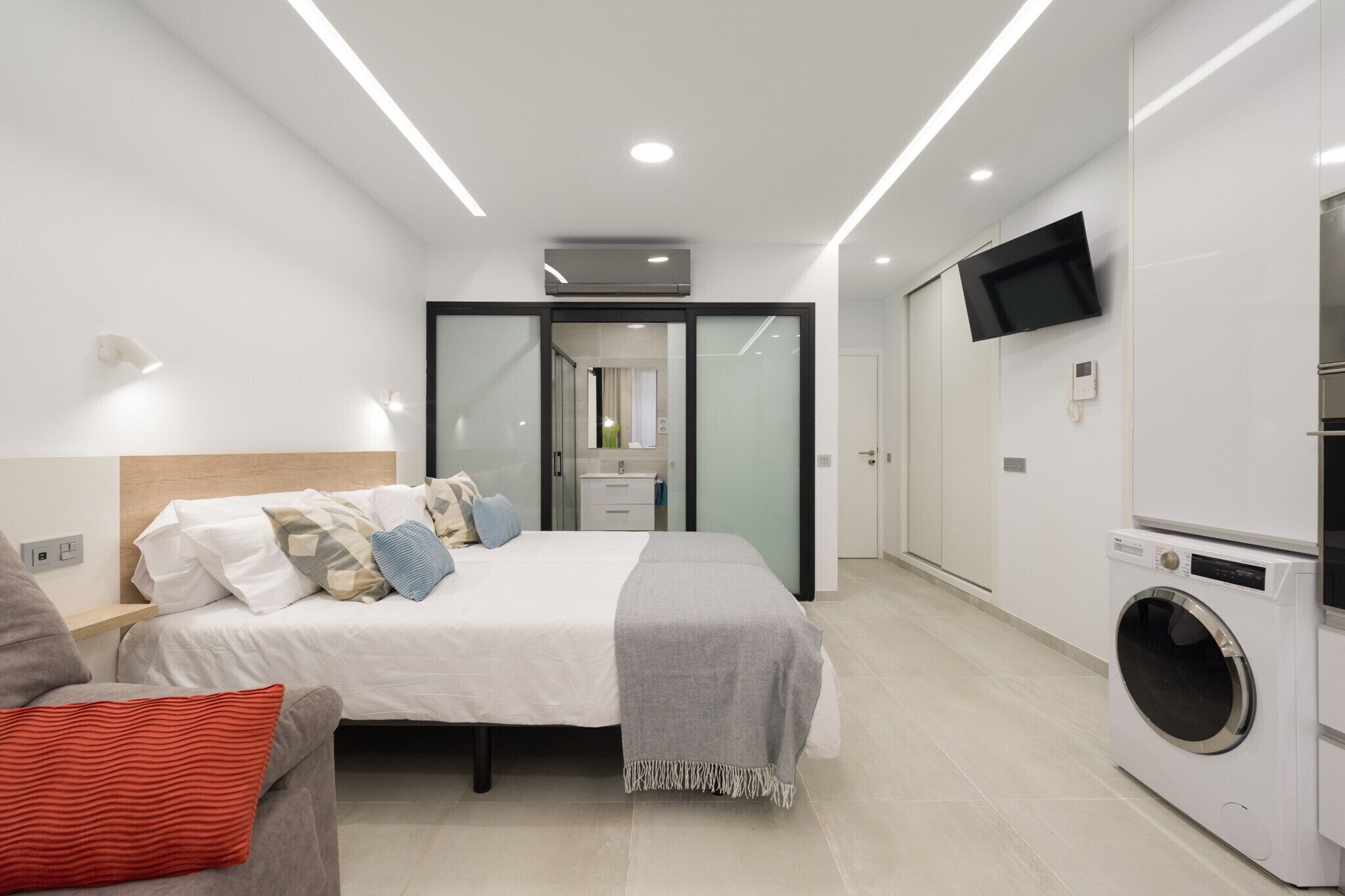 Een moderne slaapkamer met een bed, een wasmachine en een aan de muur bevestigde televisie.