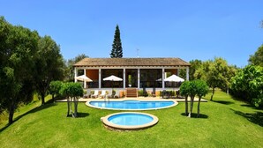 Une grande maison avec une piscine, entourée d’une pelouse bien entretenue et d’arbres.