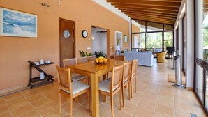 Un grand espace dédié à la salle à manger, avec une table et des chaises en bois, un chariot à café et une vue sur l’extérieur grâce à de grandes fenêtres.