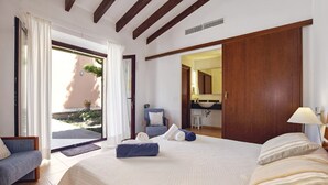Une chambre à coucher avec un grand lit, une chaise, un bureau et une salle de bain visible à travers une porte ouverte.