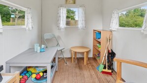 Une petite pièce bien éclairée, avec une table, une chaise, une étagère remplie de jouets et une fenêtre avec des rideaux.