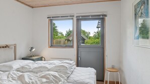 Une chambre à coucher comprenant un lit, un bureau, une chaise et une fenêtre donnant sur un paysage verdoyant avec une maison.