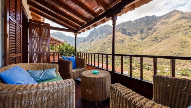Un balcone con mobili in vimini, vista sulle montagne e soffitto in legno.