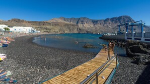 Una spiaggia con un molo di legno, un litorale roccioso e montagne sullo sfondo.