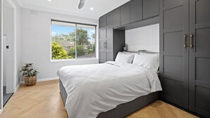 Un dormitorio moderno con una cama grande, un ventilador de techo y una ventana con vistas a zonas verdes y edificios.