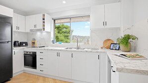 Una cocina moderna con armarios blancos, un refrigerador de acero inoxidable, un horno empotrado y una ventana con vista a la vegetación.