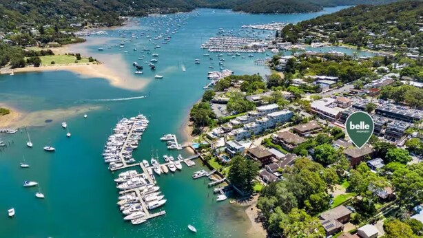 Vista aérea de un pueblo costero con un puerto deportivo lleno de barcos, rodeado de edificios residenciales y vegetación.