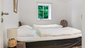 Une chambre à coucher avec un lit, une fenêtre donnant sur un paysage verdoyant, une lampe de chevet et un fauteuil.