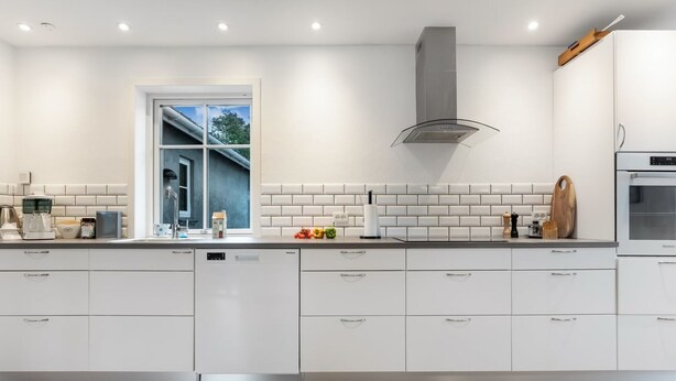 Une cuisine moderne avec des meubles blancs, un lave-vaisselle encastré, une fenêtre offrant une belle vue et une hotte de cuisinière en acier inoxydable.
