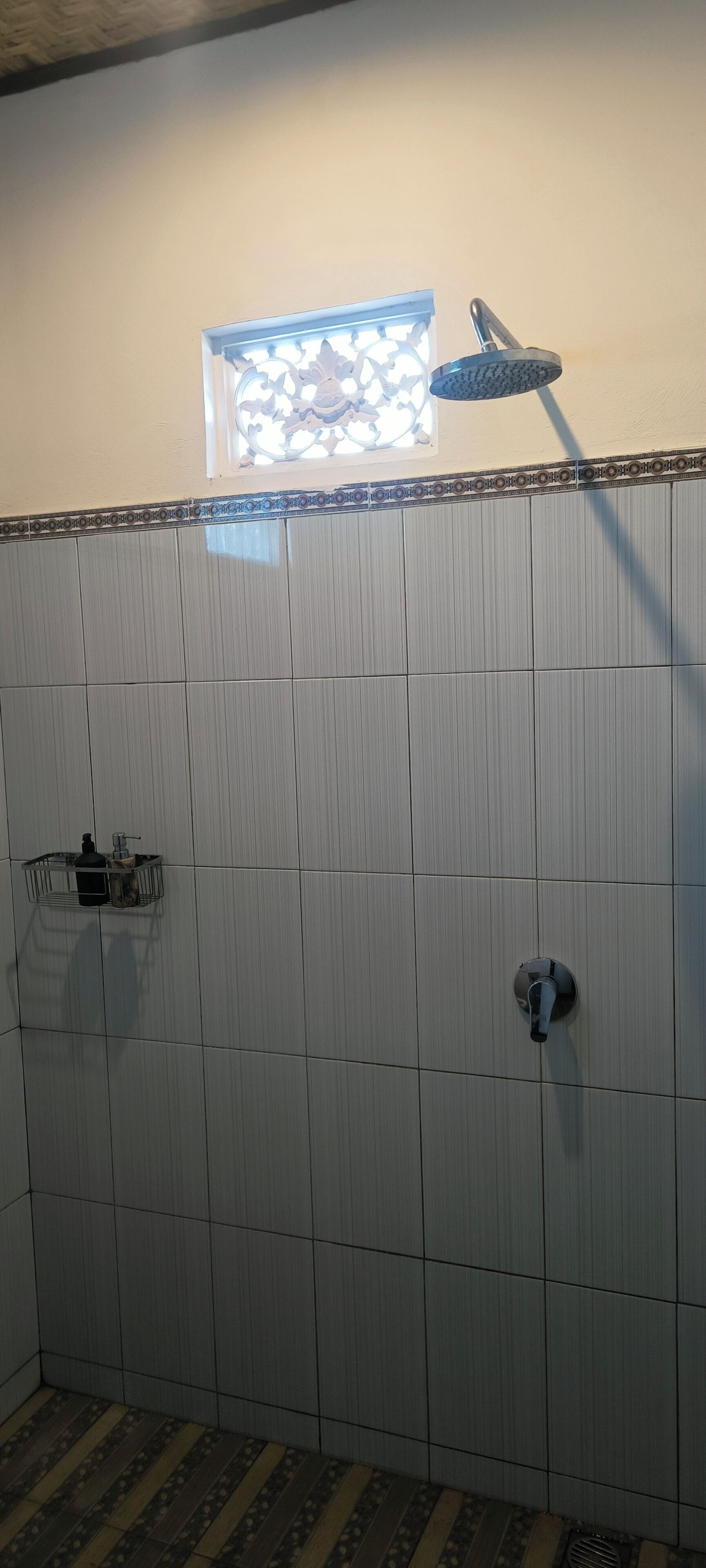 Un baño con pared de azulejos, ducha y ventana con vidrio decorativo.