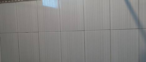 Un baño con pared de azulejos, ducha y ventana con vidrio decorativo.