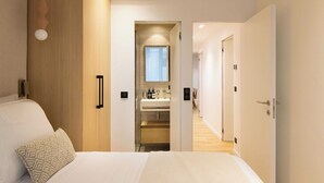 Una habitación de hotel moderna con una cama, mesita de noche y un baño visible a través de una puerta abierta.