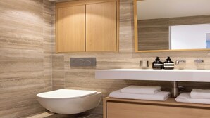 Un baño moderno con inodoro integrado, un tocador de madera con espejo y un lavamanos fijado a la pared.