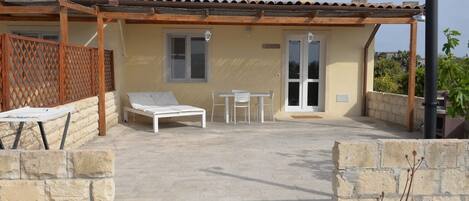 A covered outdoor area with a lounge chair, a table, and chairs.