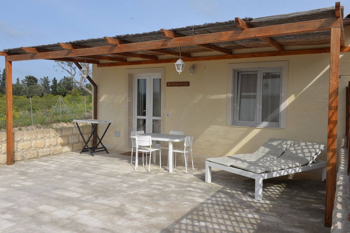 Un espace extérieur aménagé, abrité et doté d’une table et de chaises, d’un fauteuil de relaxation et d’une structure en forme de pergola.