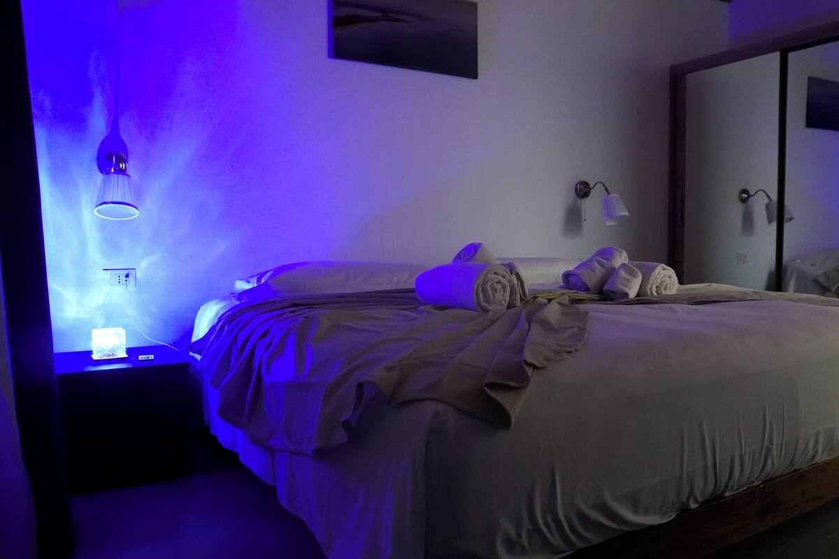 Un lit bien fait, avec des serviettes, une lampe de chevet et un luminaire fixé au mur.